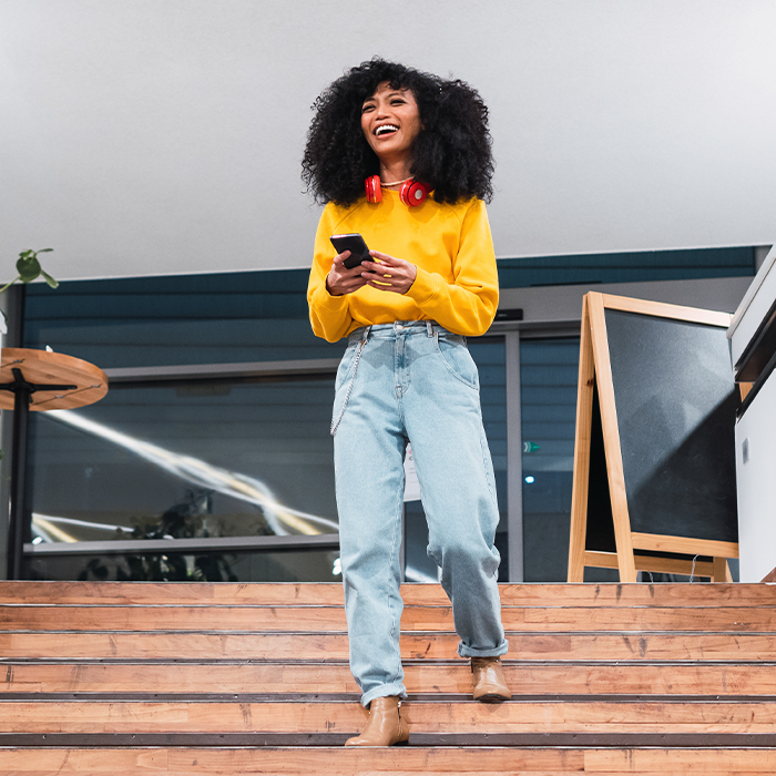 Decorative image, woman in a bright yellow sweater, large red headphones around her neck and rolled up blue jeans.