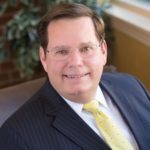 Portrait of Bryron McDanial in a navy striped blazer with a yellow tie.