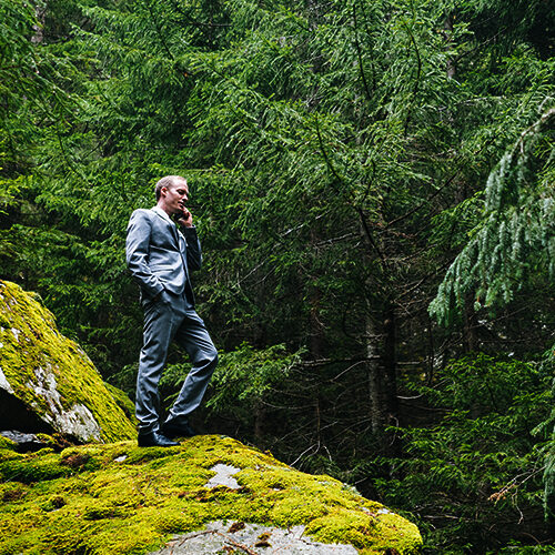 Decorative image of a business man in a grey suit taking a call on his cell phone in the forest.