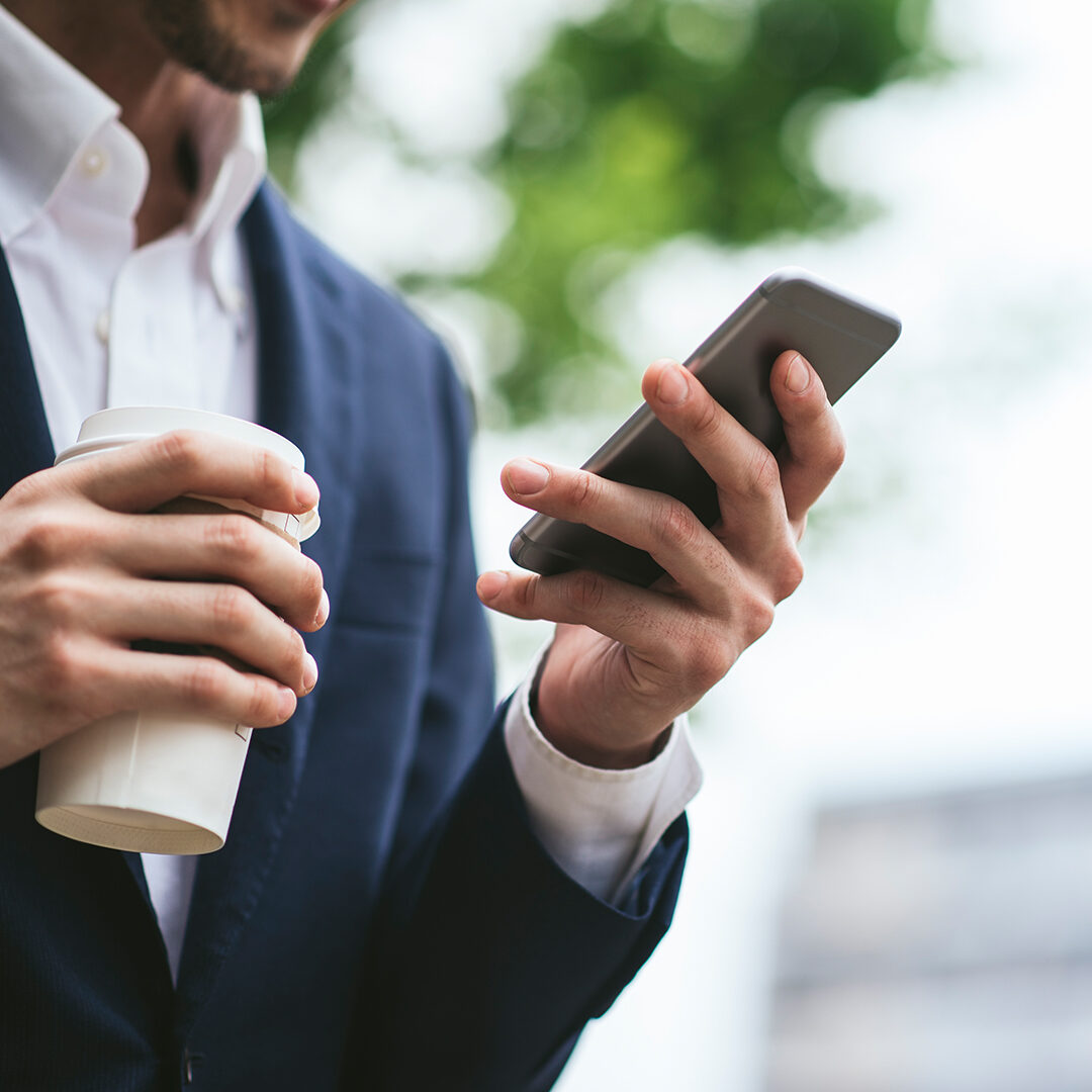 Closely cropped image of a businesman holding a phone and coffee
