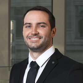 Portrait of Jordan Cameron, in a black suit, black tie and white collared shirt. Jordan has short dark brown hair.