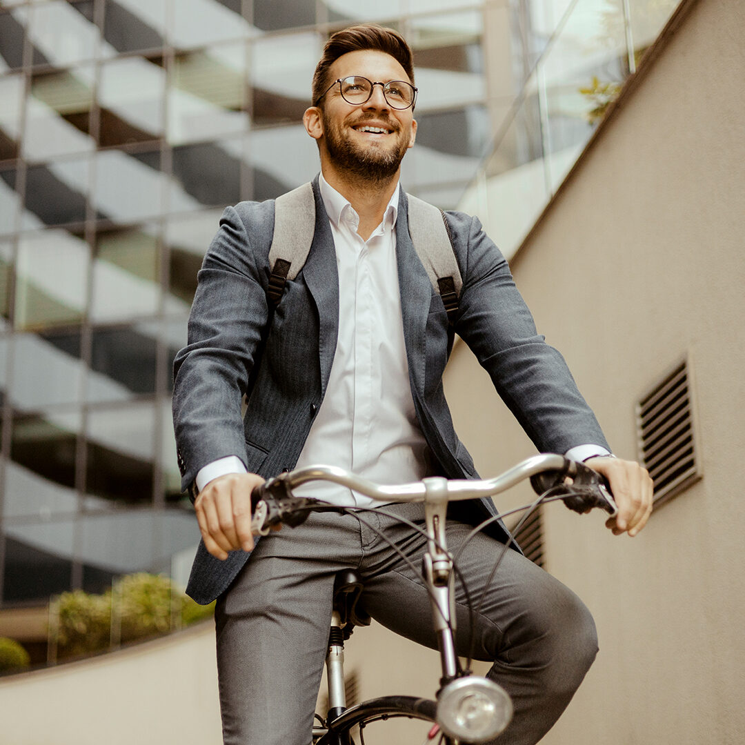 Decorative image of a man in glasses and a grey suit, riding a bike smiling.