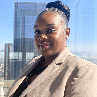 Portrait of Tawana Adams in the beige blazer, black blouse with tall office buildings in the background