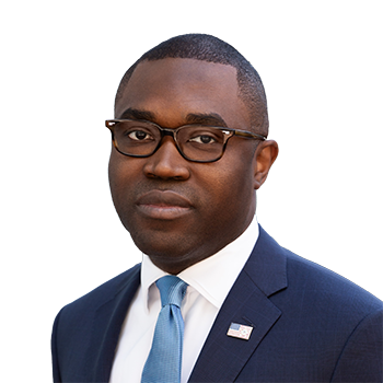 Portrait of William Yomba in a white shirt and navy blazer and american flag pin