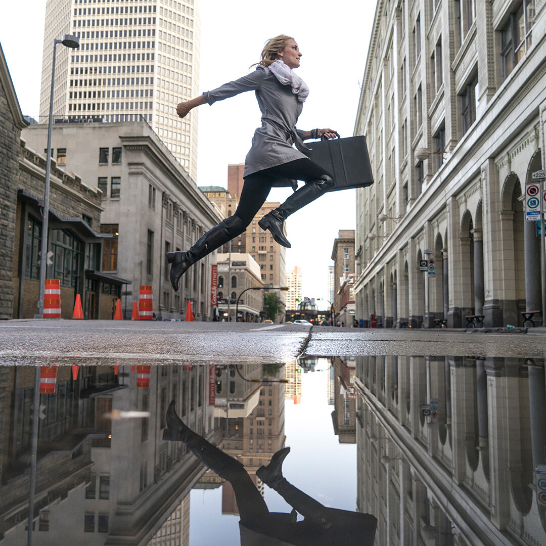 Image of a business woman jumping over a puddle downtown Calgary