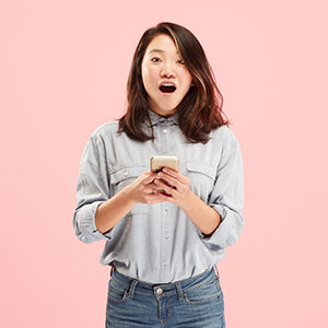 Young woman in a Canadian tuxedo with shoulder length brown hair holding her smart phone with an excited expression.