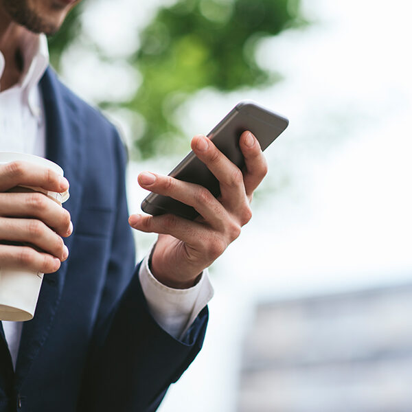 Closely cropped image of a businessman holding a phone and coffee